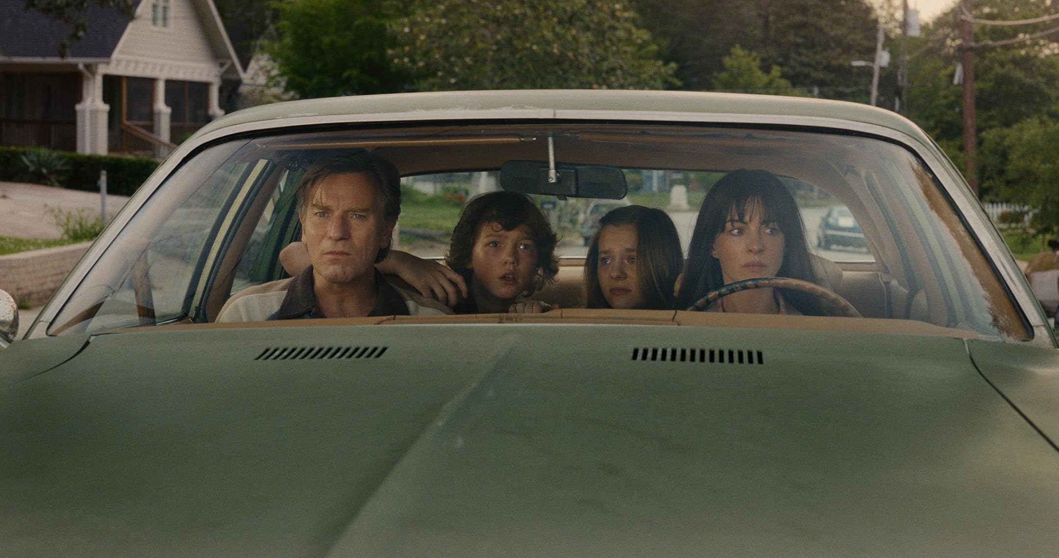 Family of four seated in a vintage car, looking ahead with concerned expressions