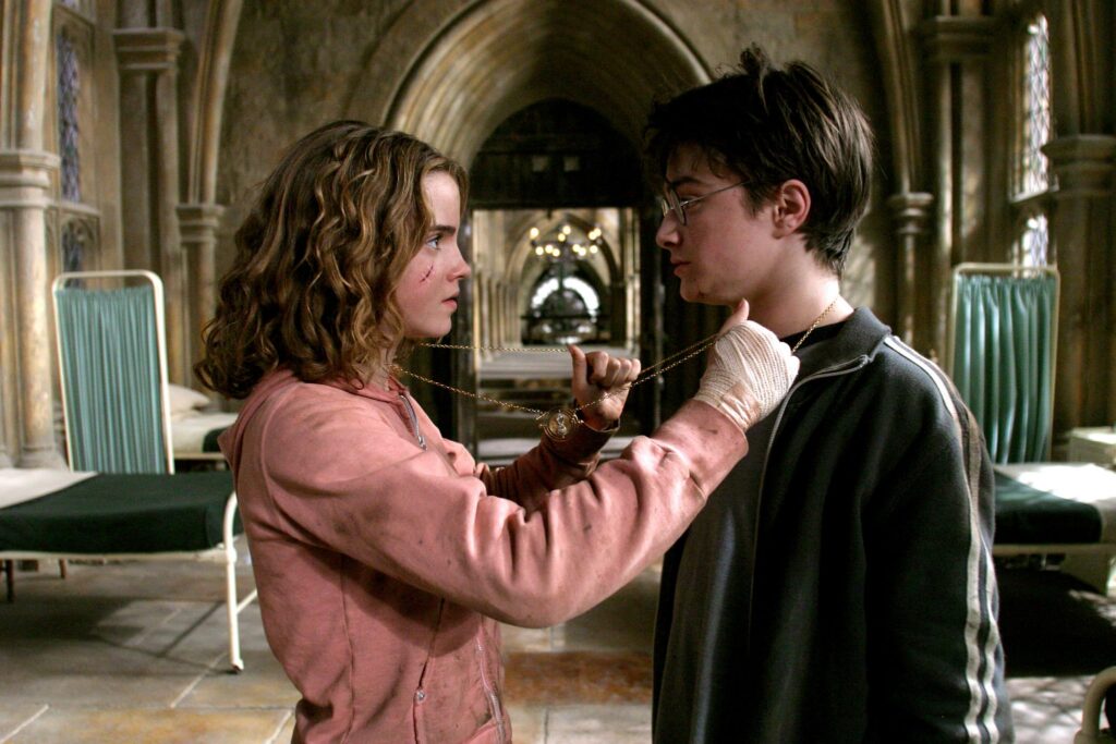 Two young people stand face to face in a cathedral-like hallway, holding a gold chain between them as if tying or presenting it.