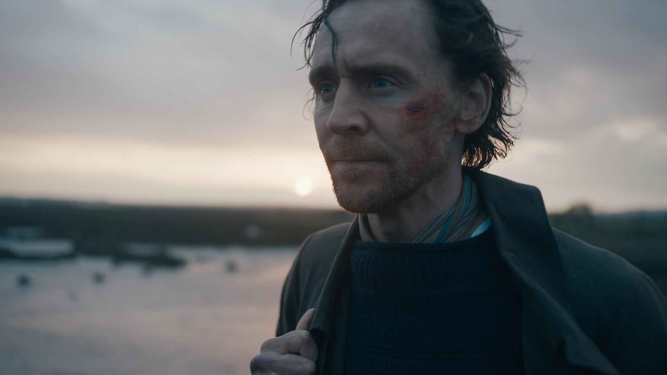 Close-up of a man with a bruised cheek looking into the distance at sunset