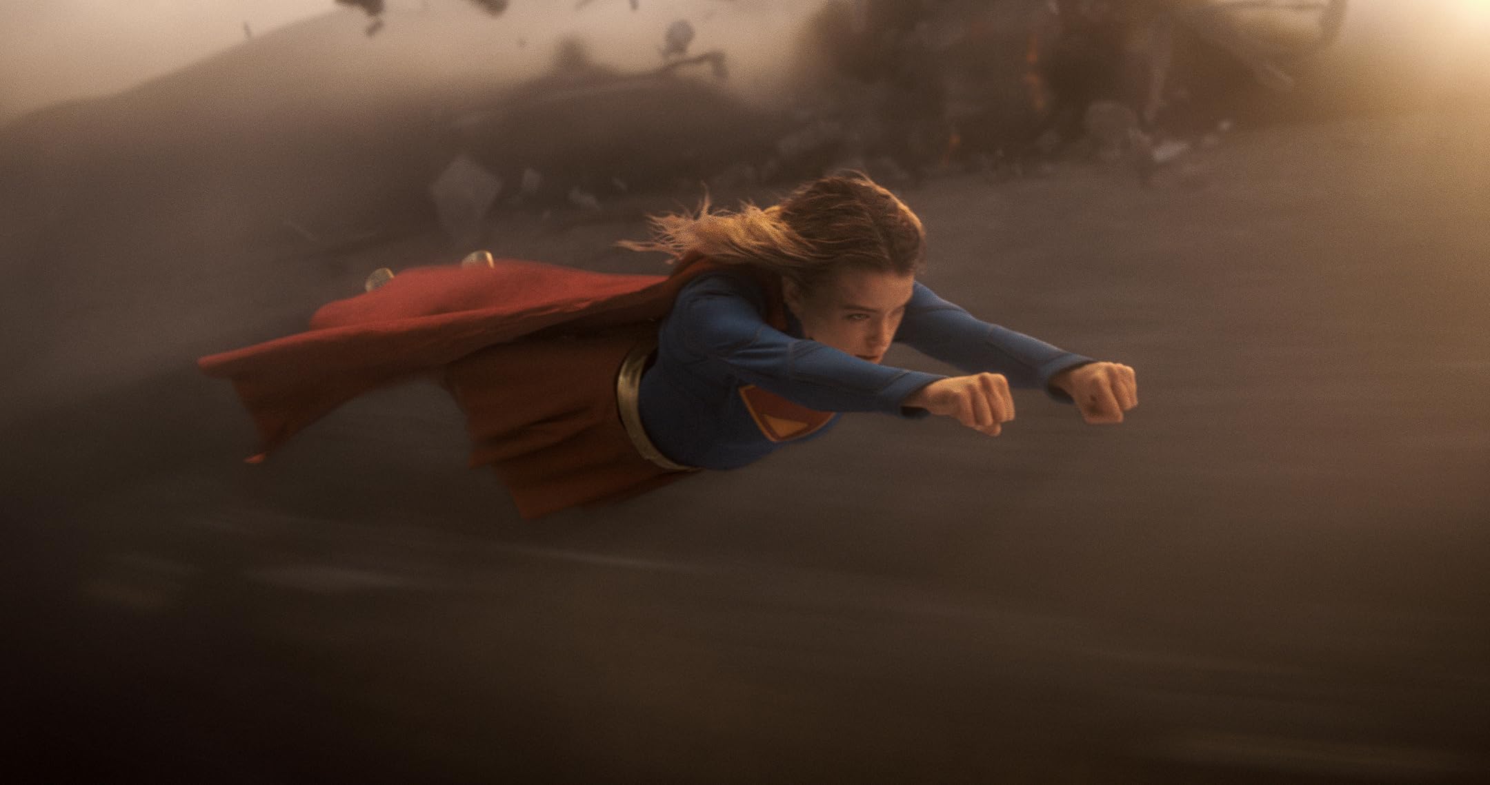 Superman-like superhero wearing blue suit and red cape flying forward with fists extended.