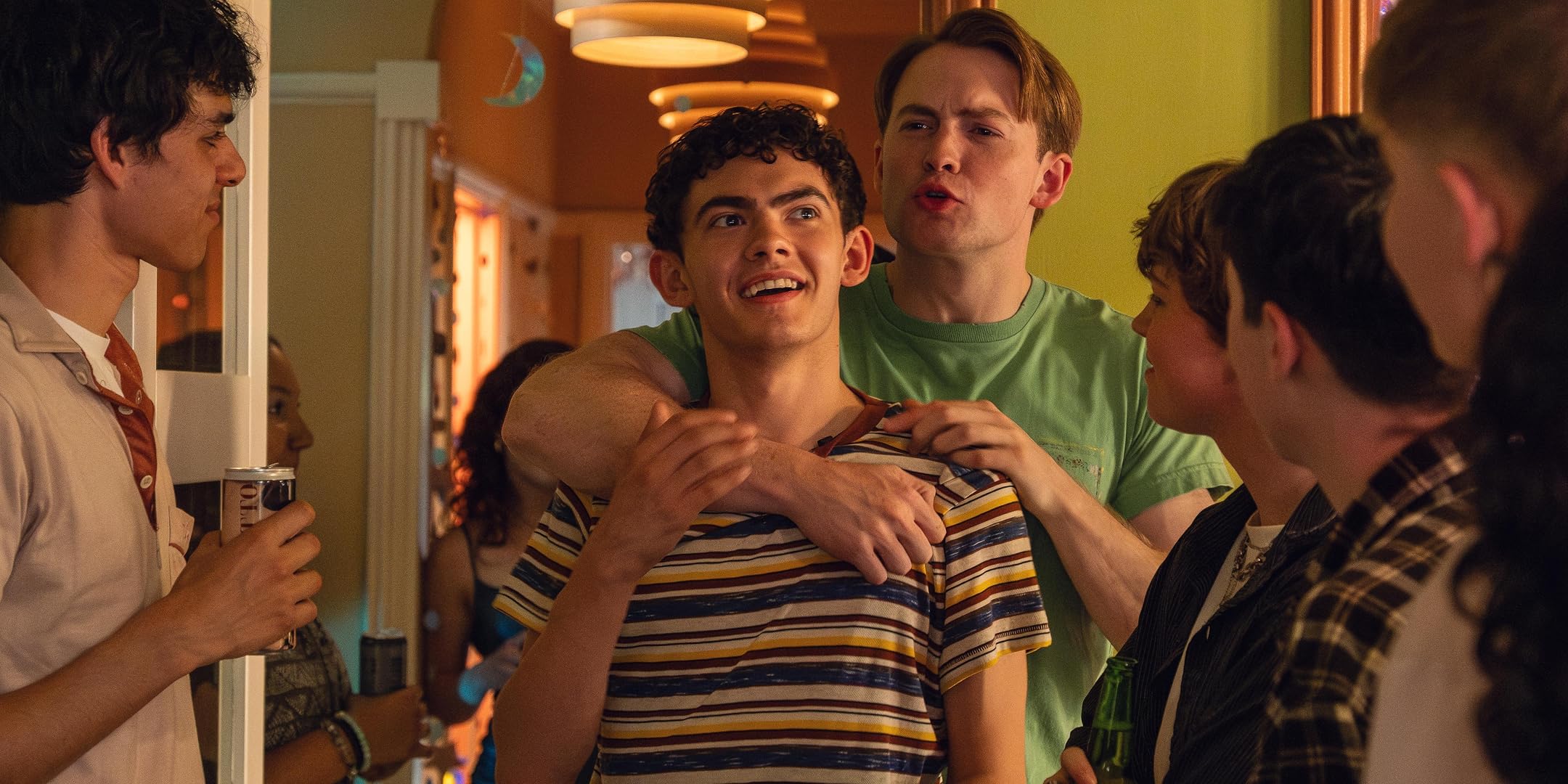 Group of friends at a party, smiling and embracing in a hallway, holding drinks and chatting.