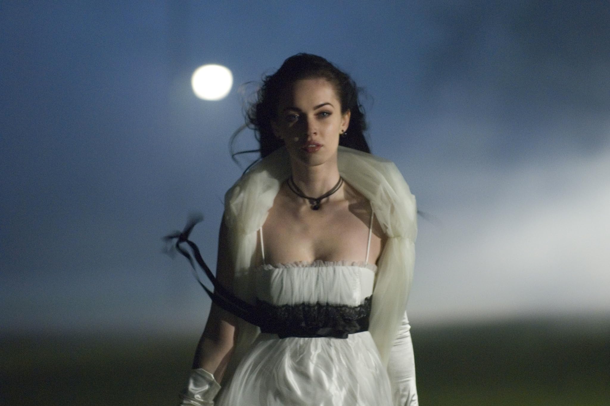 Woman in a white dress with a black belt stands at night under a bright moon in a blue sky.