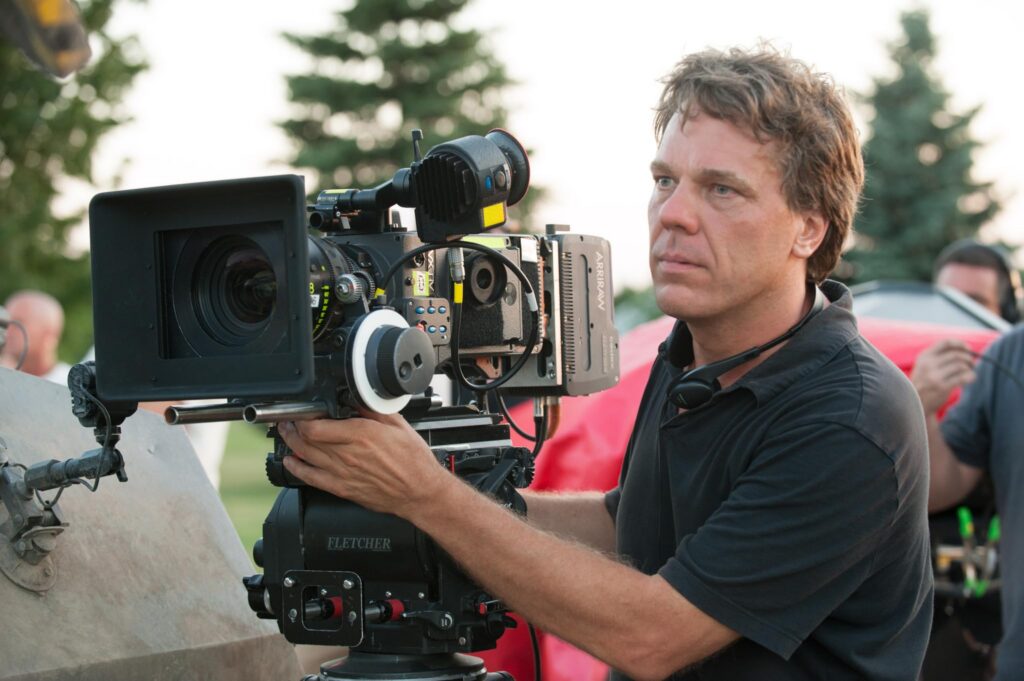 Male camera operator operating a large professional film camera outdoors, focusing on the shot.