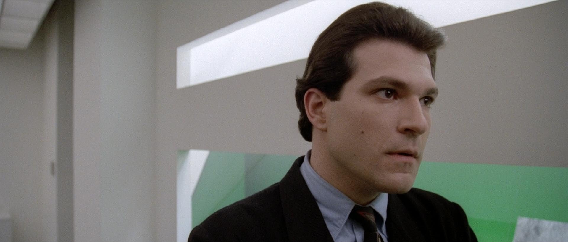 Side profile of a man in a suit and tie, indoors, looking to the right.