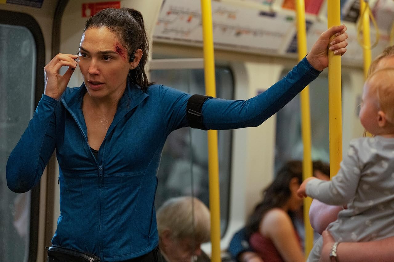 Woman on a subway wearing a blue jacket, holding a phone to her ear, gripping a yellow pole, with a bloodied cheek injury visible.