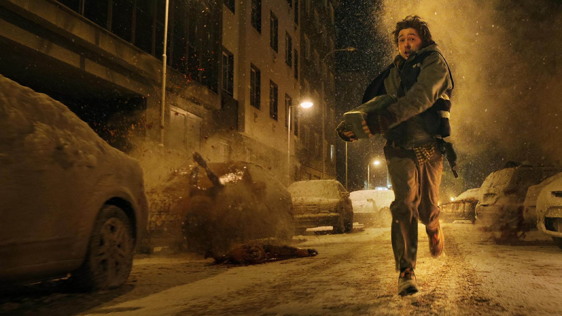 A man runs through a snowstorm on a deserted, dimly lit street at night, large snowbanks on both sides.