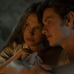 Two people cuddled close in a dimly lit setting, their faces near each other and a calm, intimate mood.