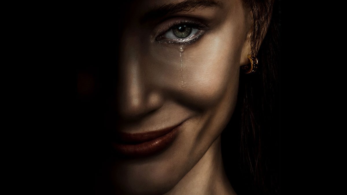 Close-up of a smiling woman's face in low light, with a single tear running down her cheek and a gold hoop earring visible.